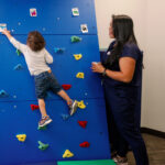 Small Child Climbing Indoor Rockwall with Supervising Teacher