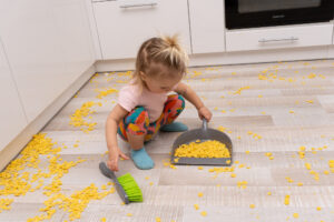 Child using Adaptive Development Skills to clean up mess on kitchen floor
